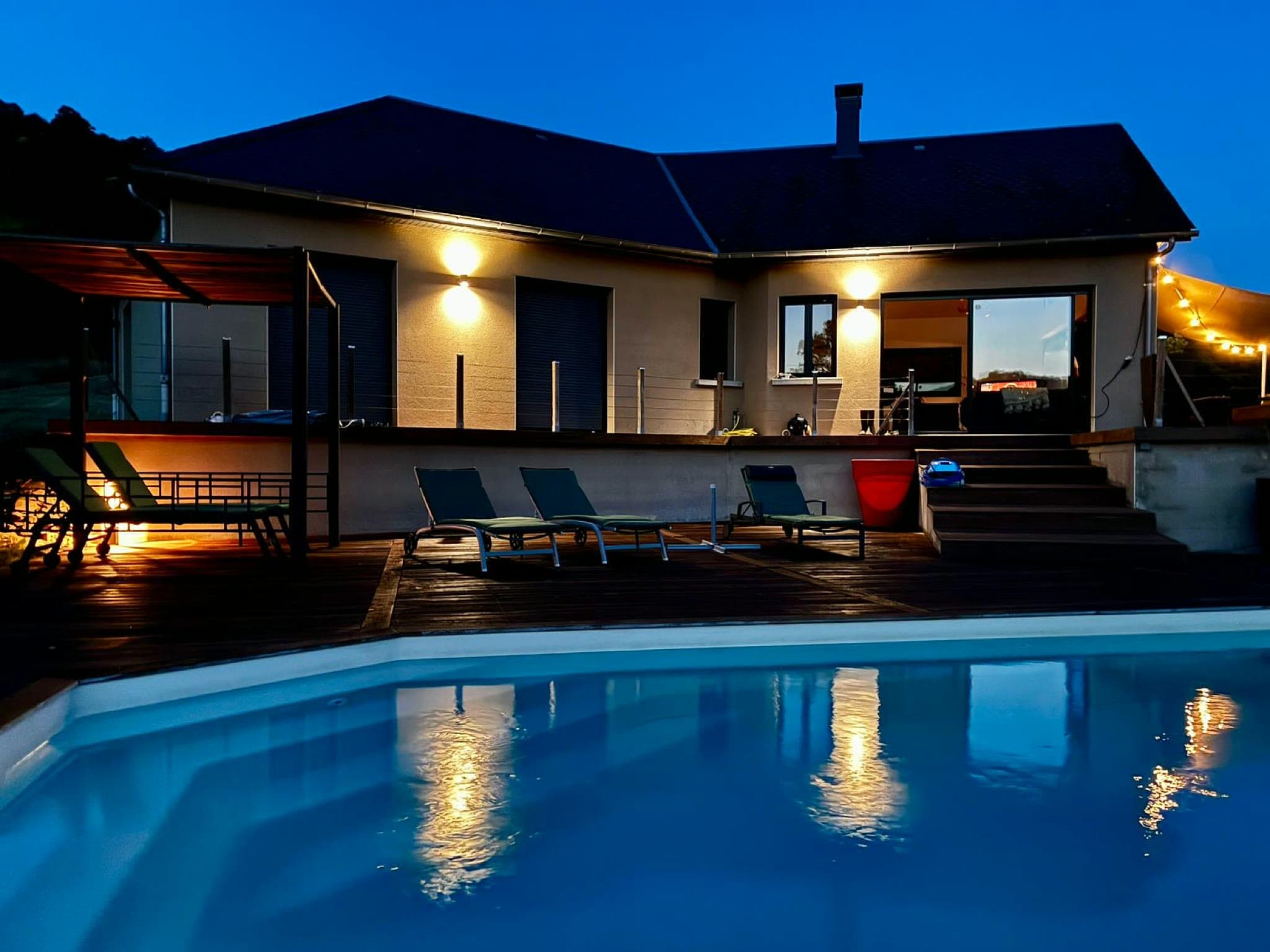 La maison illuminée et la piscine à la tombée de la nuit